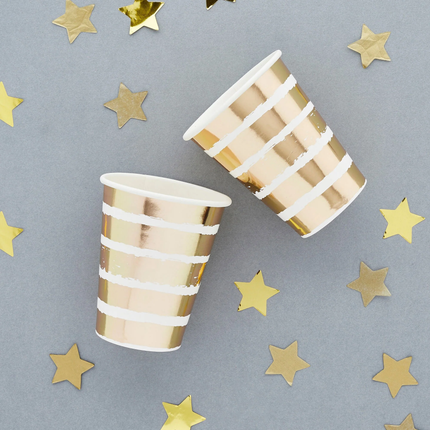 bekers met witte en gouden strepen liggen op een grijze achtergrond naast sterretjes confetti