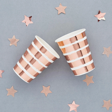 rose gouden en wit gestreepte bekers op een grijze achtergrond versierd met rose gouden sterretjes confetti