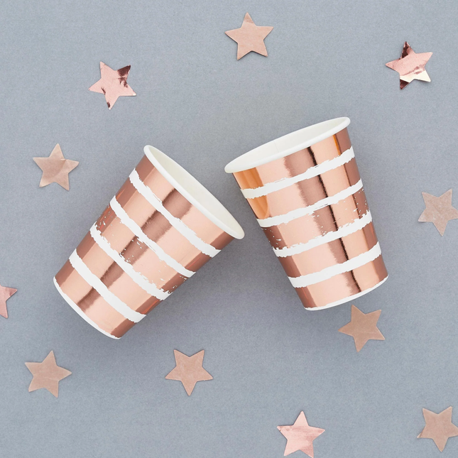 rose gouden en wit gestreepte bekers op een grijze achtergrond versierd met rose gouden sterretjes confetti