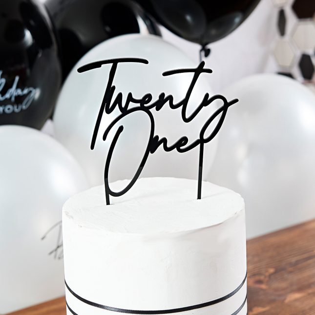 zwarte taartversiering twenty one zit in een witte taart en staat op een bruine tafel