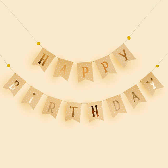 slinger met gele vlaggetjes en de gouden tekst happy birthday met witte stippen hangt voor een lichtgele achtergrond