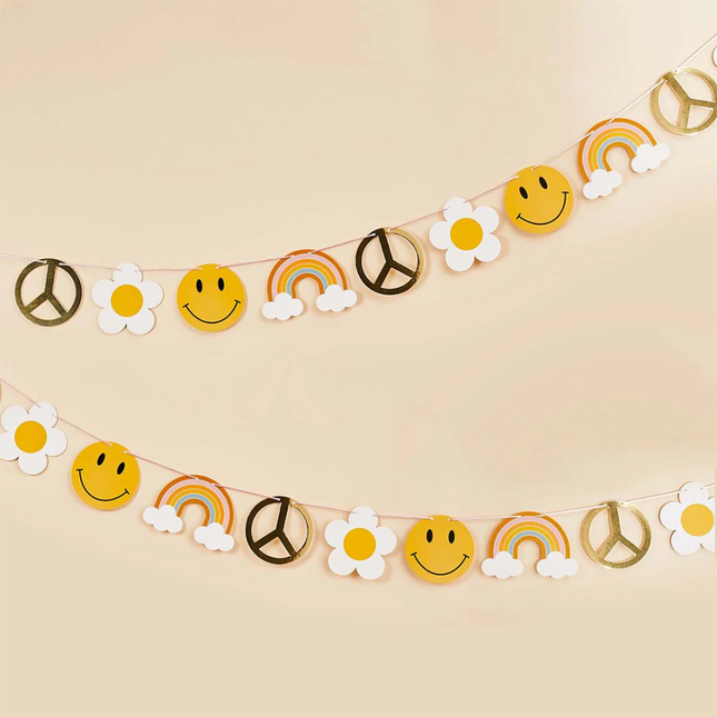 Vrolijke slinger met smileys, regenbogen, het vredesteken en madeliefjes hangt voor een perzikkleurige muur