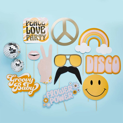 Photo booth props met een smiley, vredestekens en bordjes met hippie teksten liggen op een lichtblauwe achtergrond