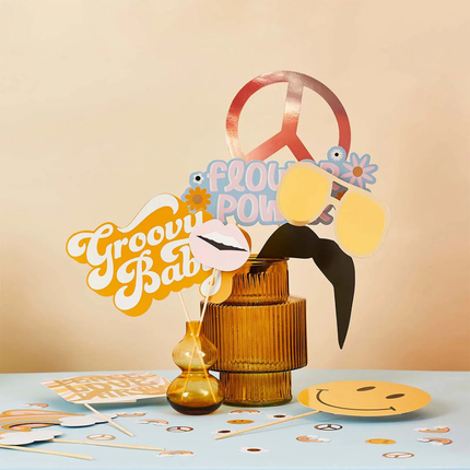 Photo booth props zitten in een bruin glazen vaasje en staan op een blauwe tafel voor een perzikkleurige muur