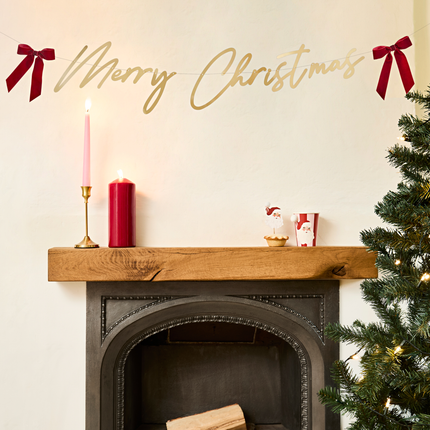 gouden merry christmas slinger met rode strikjes hangt boven houten open haard