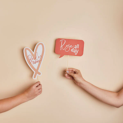 Twee handen houden bordjes vast met de tekst rose all day en she said yaaas voor een lichtgele beige muur