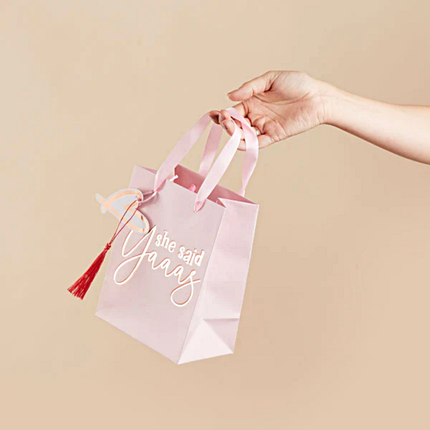 Cadeautasje wordt vastgehouden voor een perzikkleurige muur en is roze van kleur met een tassel
