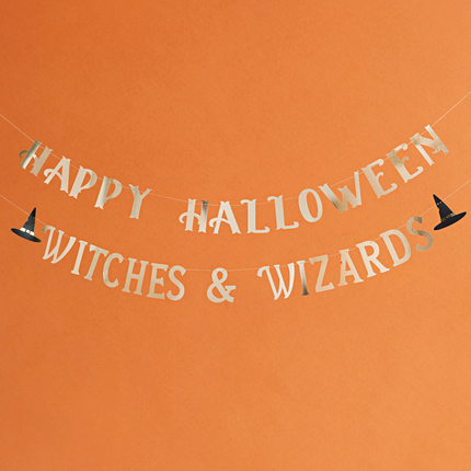 Slinger met gouden tekst happy halloween witches & wizards met een heksenhoed hangt voor een oranje achtergrond