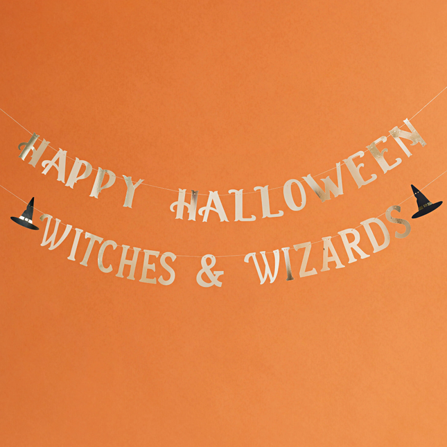 Slinger met gouden tekst happy halloween witches & wizards met een heksenhoed hangt voor een oranje achtergrond