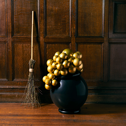 Heksenketel met bubbels in het zwart en goud staat voor een houten muur