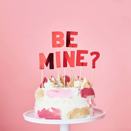 Rode taarttopper met de tekst be mine? zitten in een witte taart voor een lichtroze achtergrond