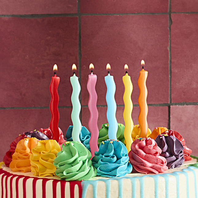verjaardagskaarsjes in het geel, blauw, rood, oranje, groen en roze zitten in een regenboog drip taart