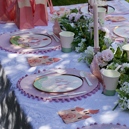 Tafel versierd met een roze tiara, bordjes met een koets erop en cadeautasjes in de vorm van een koets naast een bloemenslinger en een lange kaars