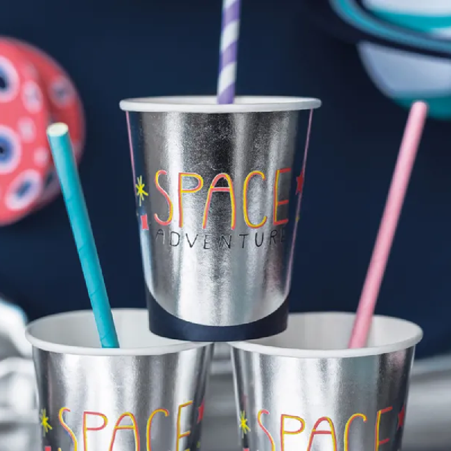 Metallic bekers met de tekst 'space party' staan als een piramide op elkaar voor een donkerblauwe muur