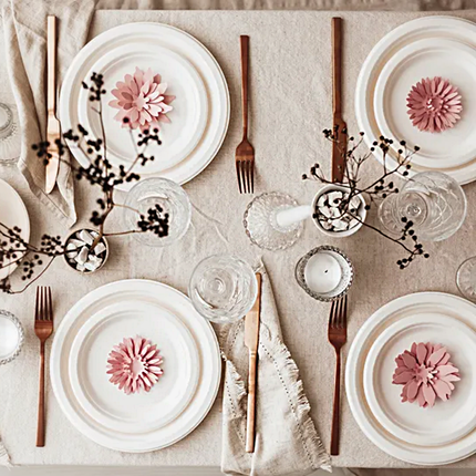 Tafel versierd met goud bestek, witte borden en roze bloemen