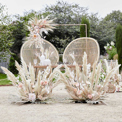 rotan stoelen die buiten voor een rechthoekig frame staat met pampa pluimen
