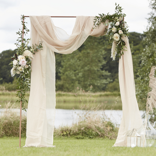 taupe drapeerdoek over een rose gouden boog staat voor een meer en is versierd met groene planten en witte bloemen