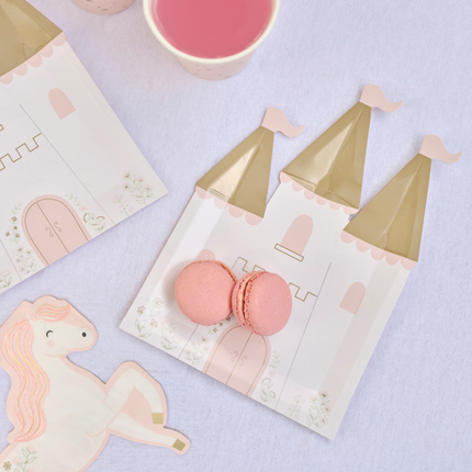 Papieren bordjes in de vorm van een kastel met gouden torens en bloemen ligt op een paarse tafel versierd met roze macarons