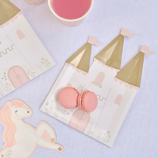 Papieren bordjes in de vorm van een kastel met gouden torens en bloemen ligt op een paarse tafel versierd met roze macarons