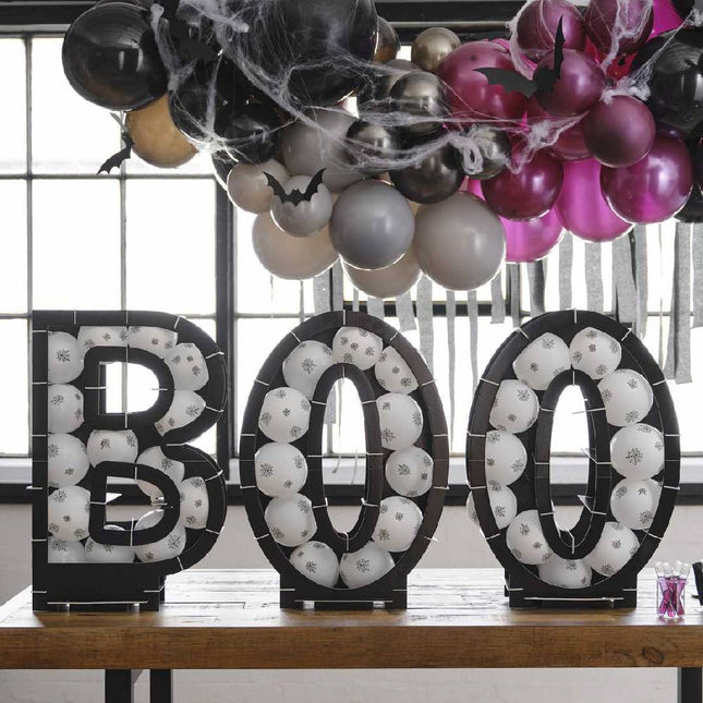 Ballonnen standaard in de vorm van de letters BOO gevuld met witte ballonnen bedrukt met spinnenwebben op tafel