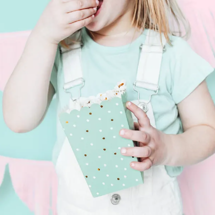Meisje in witte overall houd een mintgroen bakje vast gevuld met popcorn