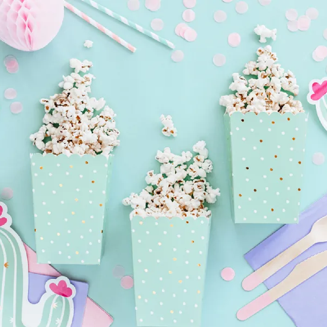 Drie mintgroene bakjes met witte en gouden stippen zijn gevuld met popcorn en liggen op een mintgroene tafel