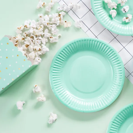 Mintgroene papieren bordjes liggen op tafel omringd door popcorn en een mintgroen popcornbakje met gouden en witte stippen