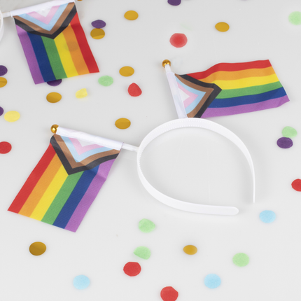 witte haarband met regenboog vlaggetjes ligt op een wit kleed met regenboog confetti