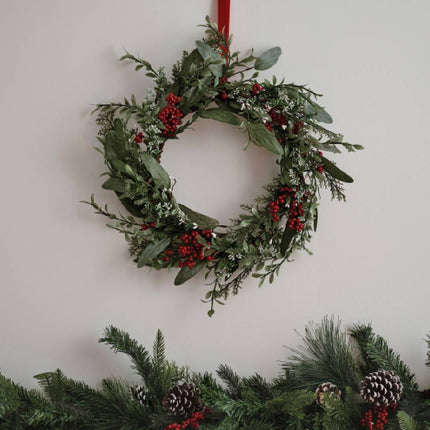 Kerstkrans aan rood lint met rode besjes met daaronder een kerstslinger
