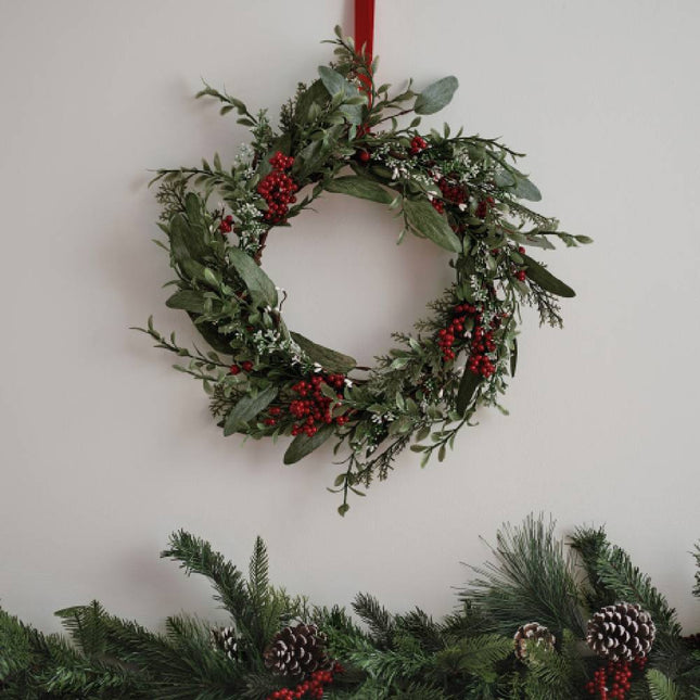 Kerstkrans aan rood lint met rode besjes met daaronder een kerstslinger