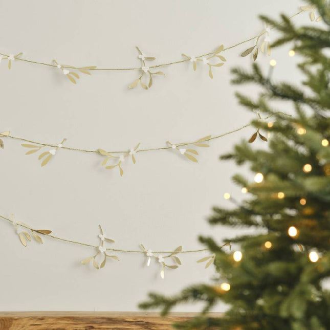 Kerstboom met daarvoor een slinger met gouden hulsttakjes eraan