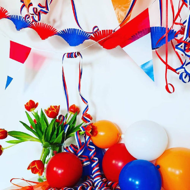 Vlaggetjes in de kleuren rood, wit en blauw hangen boven een tafel met oranje, rode, blauwe en witte ballonnen en een vaasje met oranje tulpen