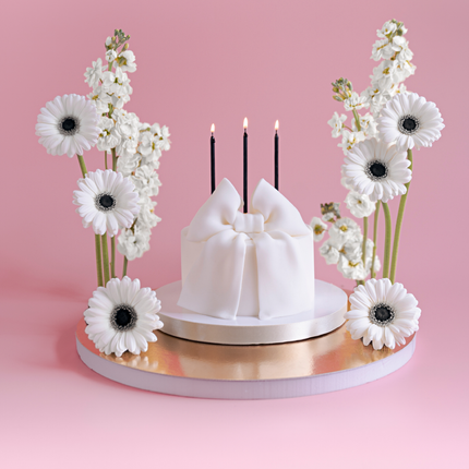 witte taart versierd met een strik en zwarte kaarsjes staat op een gouden plateau versierd met wit en zwarte bloemen