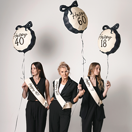drie vrouwen in zwarte pakken met creme sjerp met de teksten happy 18, happy 40 en happy 60