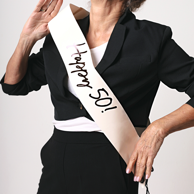 creme sjerp met de tekst happy 50 in het zwart wordt gedragen door een vrouw met een witte hartjesbril en zwarte blazer