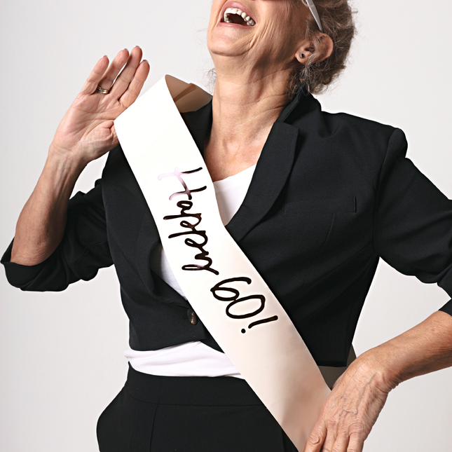 creme sjerp met de tekst happy 60 in het zwart wordt gedragen door een vrouw met een witte hartjesbril en zwarte blazer