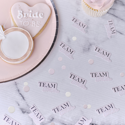 Tafelconfetti met roze cirkels en roze confetti met de tekst team bride in het zwart en wit ligt op een marmeren tafel