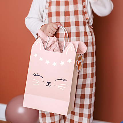 roze cadeautas met een gouden katten gezichtje word vastgehouden door een meisje in een rood met wit geblokte tuinbroek