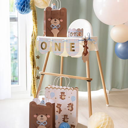 een bruine cadeautas met een beer en een creme cadeautas met beertjes met blauwe feesthoedjes op staan op tafel