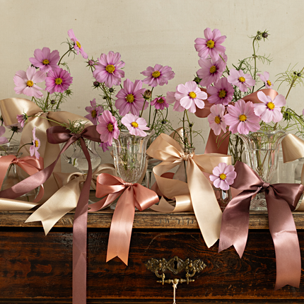 houten tafel versierd met vaasjes met bloemen en satijnlint in het roze en goud