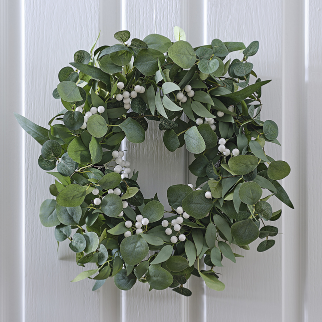 Krans met eucalyptusbladeren en witte besjes hangt aan een witte, houten deur