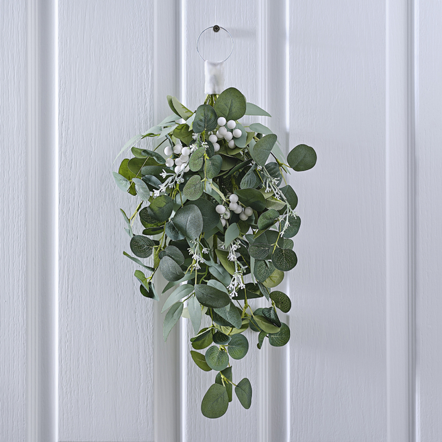 Eucalyptus hanger met witte besjes en takken hangt aan een witte, houten deur