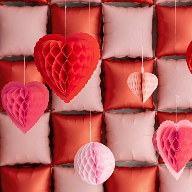 honeycombs in de vorm van hartjes hangen voor een roze met roze backdrop