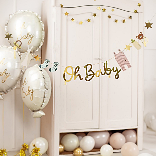 Slinger met de gouden tekst 'oh baby' hangt n een babykamer met beige en creme ballonnen en gouden sterretjes