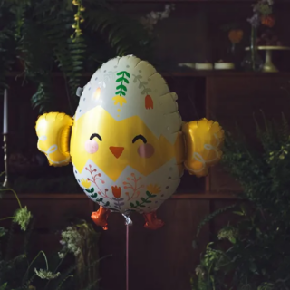 Folieballon in de vorm van een kuiken zweeft in een donkere ruimte versierd met donkergroene bladeren