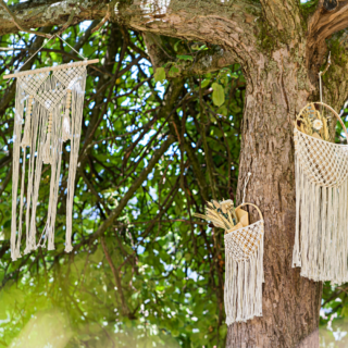 Macrame zakjes en hanger hangen aan een boom en zijn gevuld met bloemen