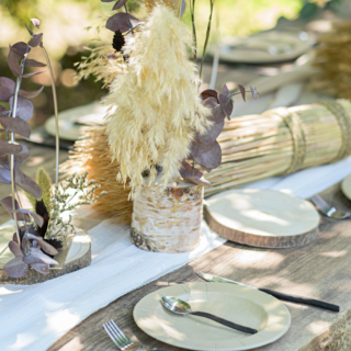 Houten tafel staat buiten en is versierd met droogbloemen, veren en boomstammen