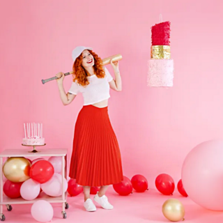 vrouw met rode rok staat in een roze ruimte met een lippenstift pinata en rode, rode en gouden ballonnen