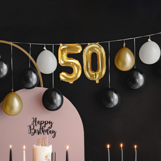 ballonnenslinger met cijferballonnen 50 in het zwart, goud en wit hangt voor een zwarte muur boven roze en zwarte versiering