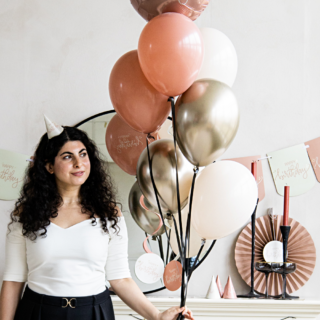 een vrouw met zwarte krullen houd een bos met roze en beige ballonnen vast